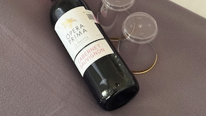 A bottle of wine with a red cap and a label, placed on a table with rose petals scattered around. - Casa Selva Arte Bacalar Free Bikes & Kayaks (Bacalar)