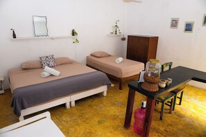A room with two beds, a wooden cabinet, a table with a basket and jars, and a chair.