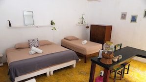 A room with two beds, a wooden cabinet, a table with a basket and jars, and a chair. - Casa Selva Arte Bacalar Free Bikes & Kayaks (Bacalar)