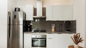 A modern kitchen with stainless steel appliances, white cabinetry, and a small wooden table with a vase. - Cana Brava Residences | Panoramic Condo | Golf View (Punta Cana)