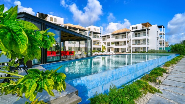 A modern hotel with a swimming pool, outdoor seating, and a clear blue sky. - Cana Brava Residences | Panoramic Condo | Golf View (Punta Cana)