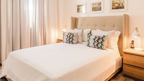 A neatly made bed with a white bedspread and multiple pillows, a ceiling fan, a bedside lamp, and a wall-mounted air conditioner. - Cana Brava Residences | Panoramic Condo | Golf View (Punta Cana)