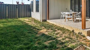Een modern huis met een overdekte patio, een omheinde achtertuin en een kleine tuin.