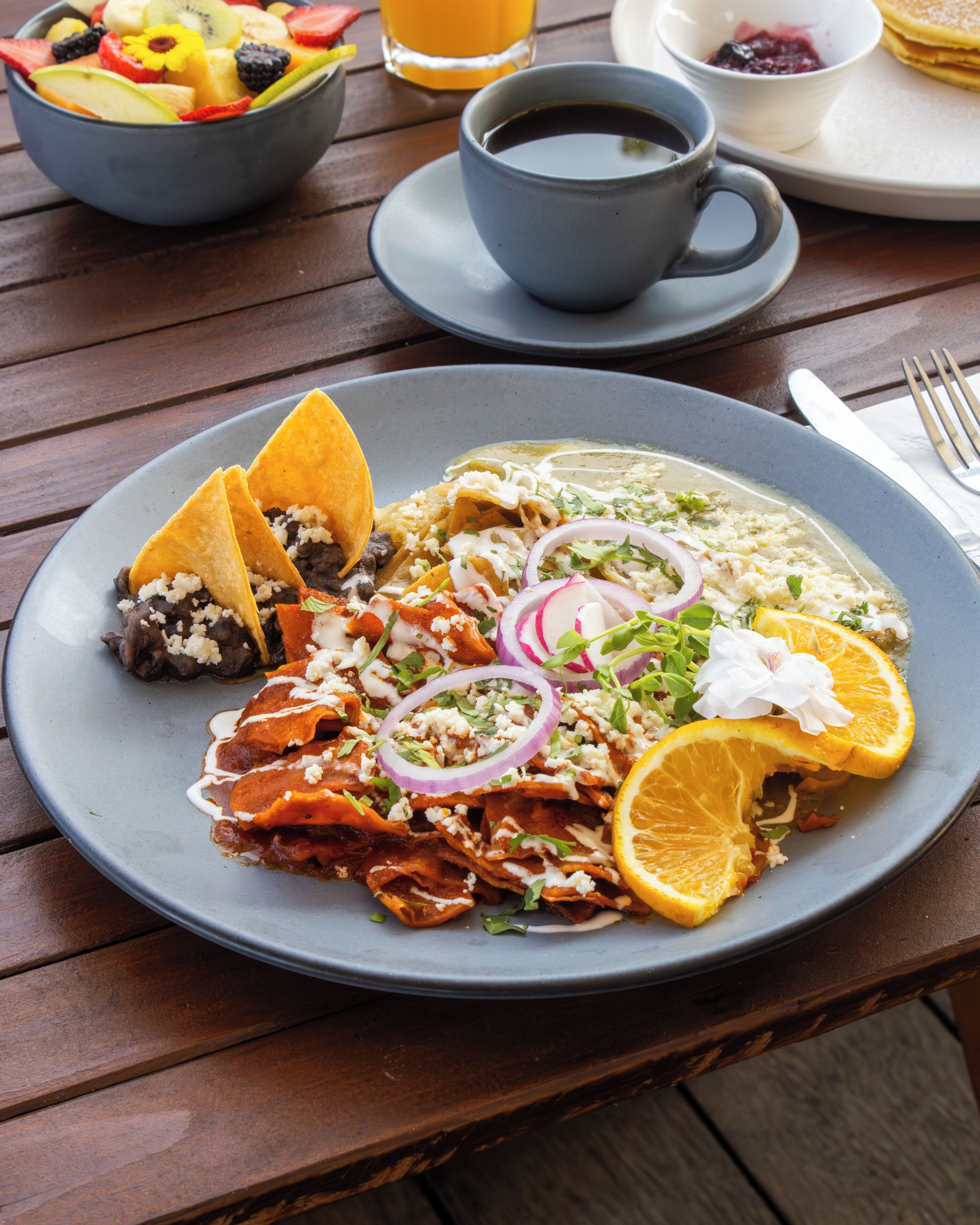 Una mesa de comedor con un plato de comida, una taza de café y un bol de fruta.