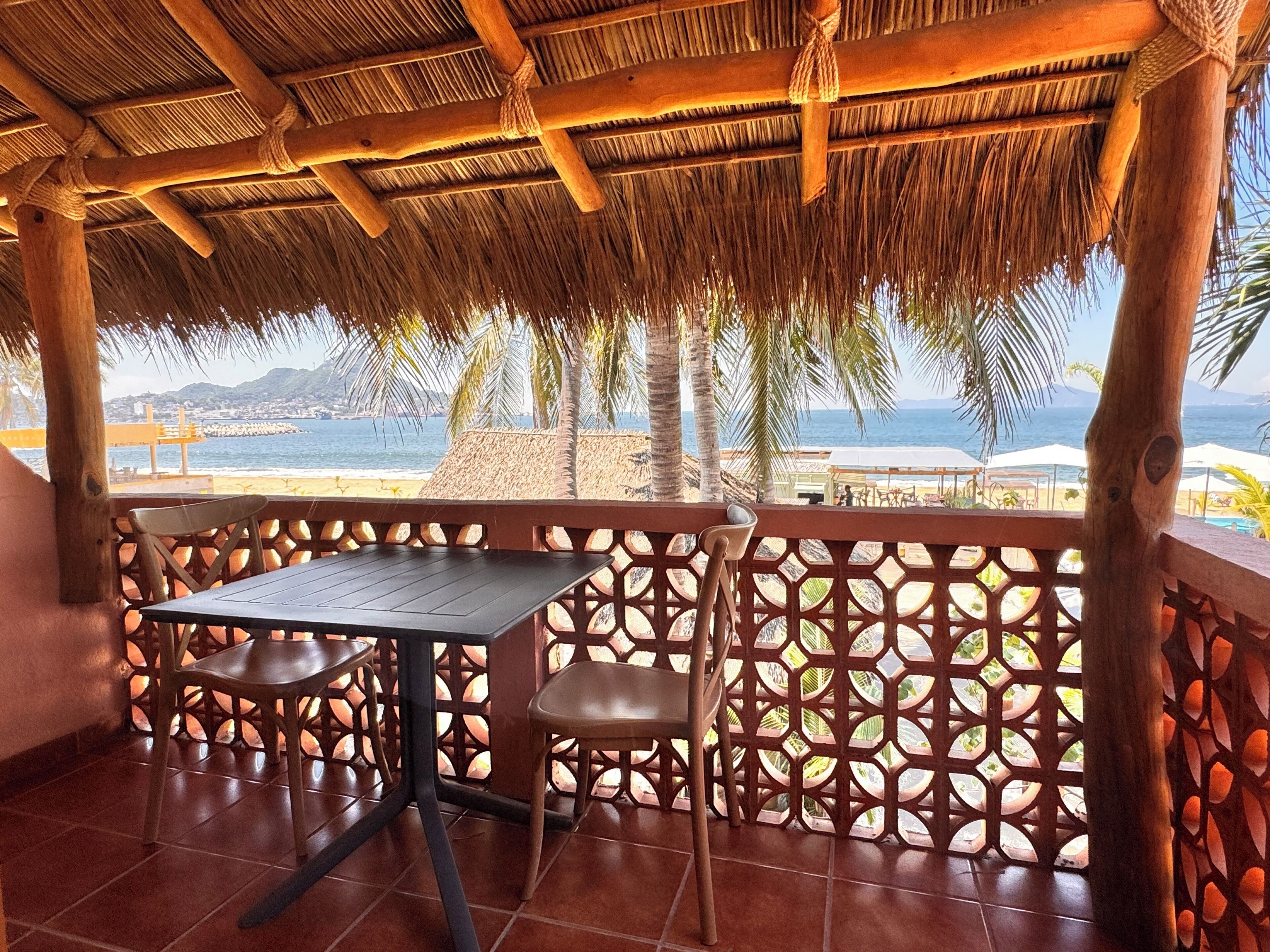 Un espacio de estar al aire libre techado con una mesa y sillas, con vistas a una playa y al océano.