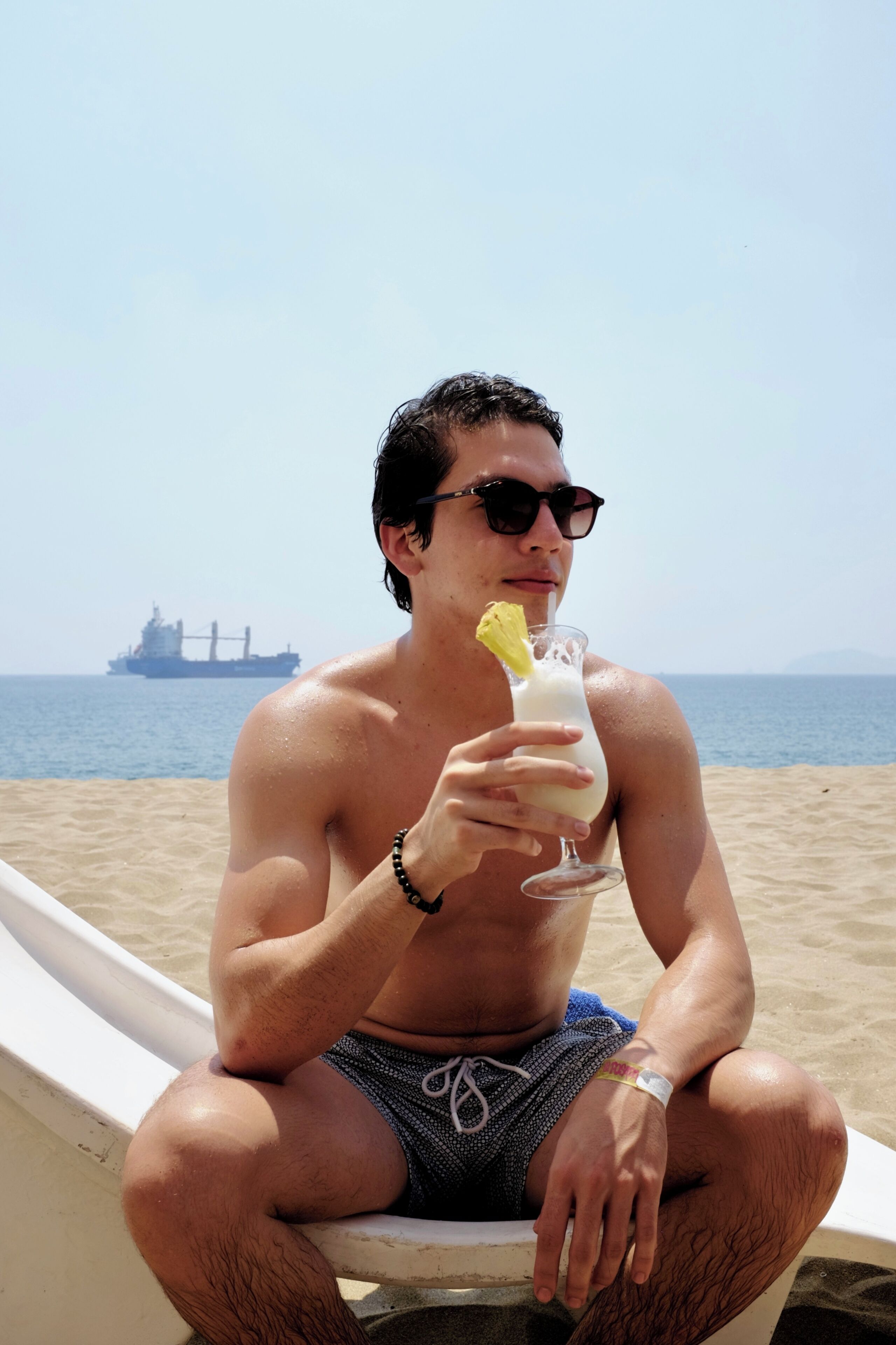 Una persona sentada en un bote en la playa, con un barco al fondo.