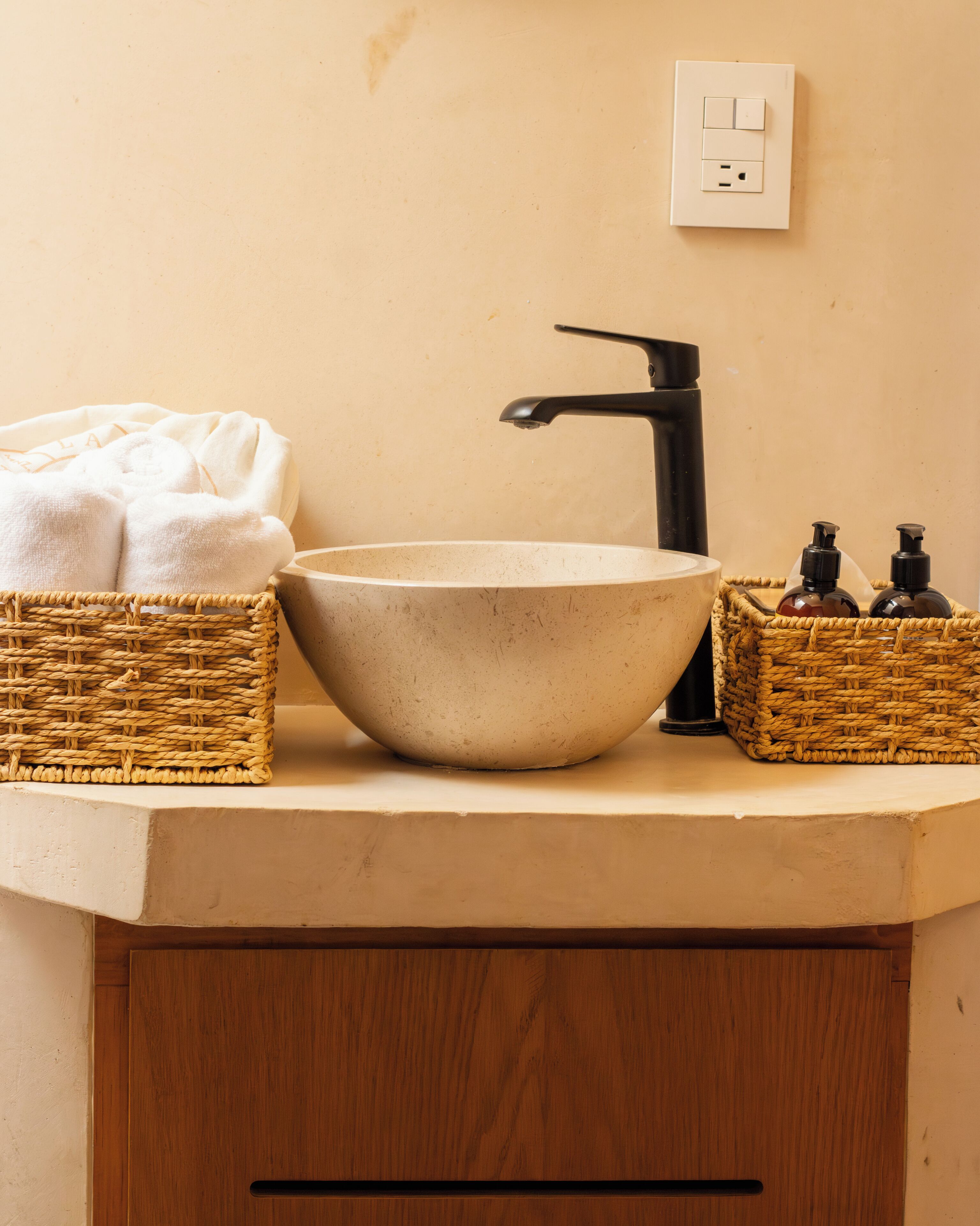 A bathroom with a beige sink, black faucet, and two wicker baskets on the countertop.