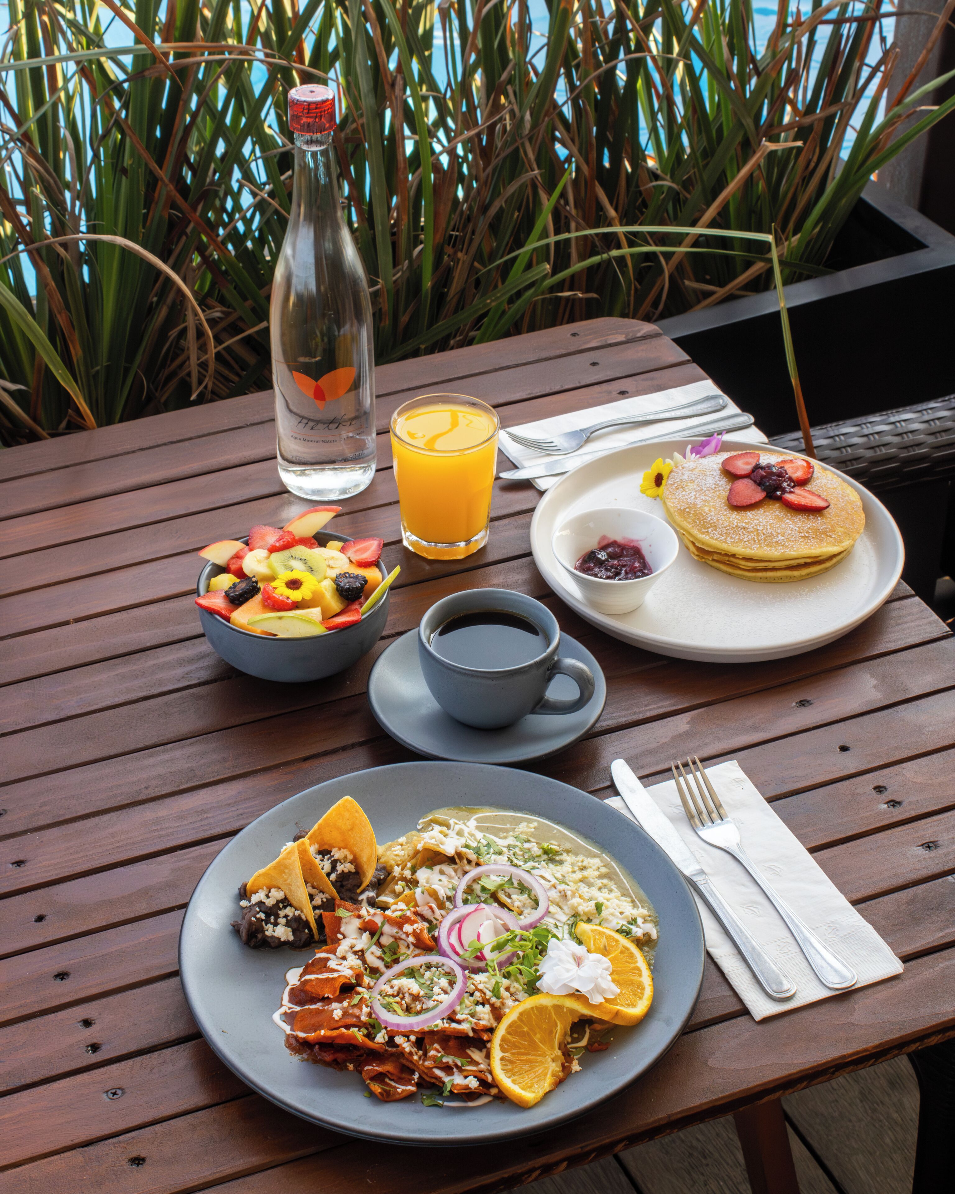 Una mesa de madera con alimentos para el desayuno, como panqueques, fruta y una bebida.