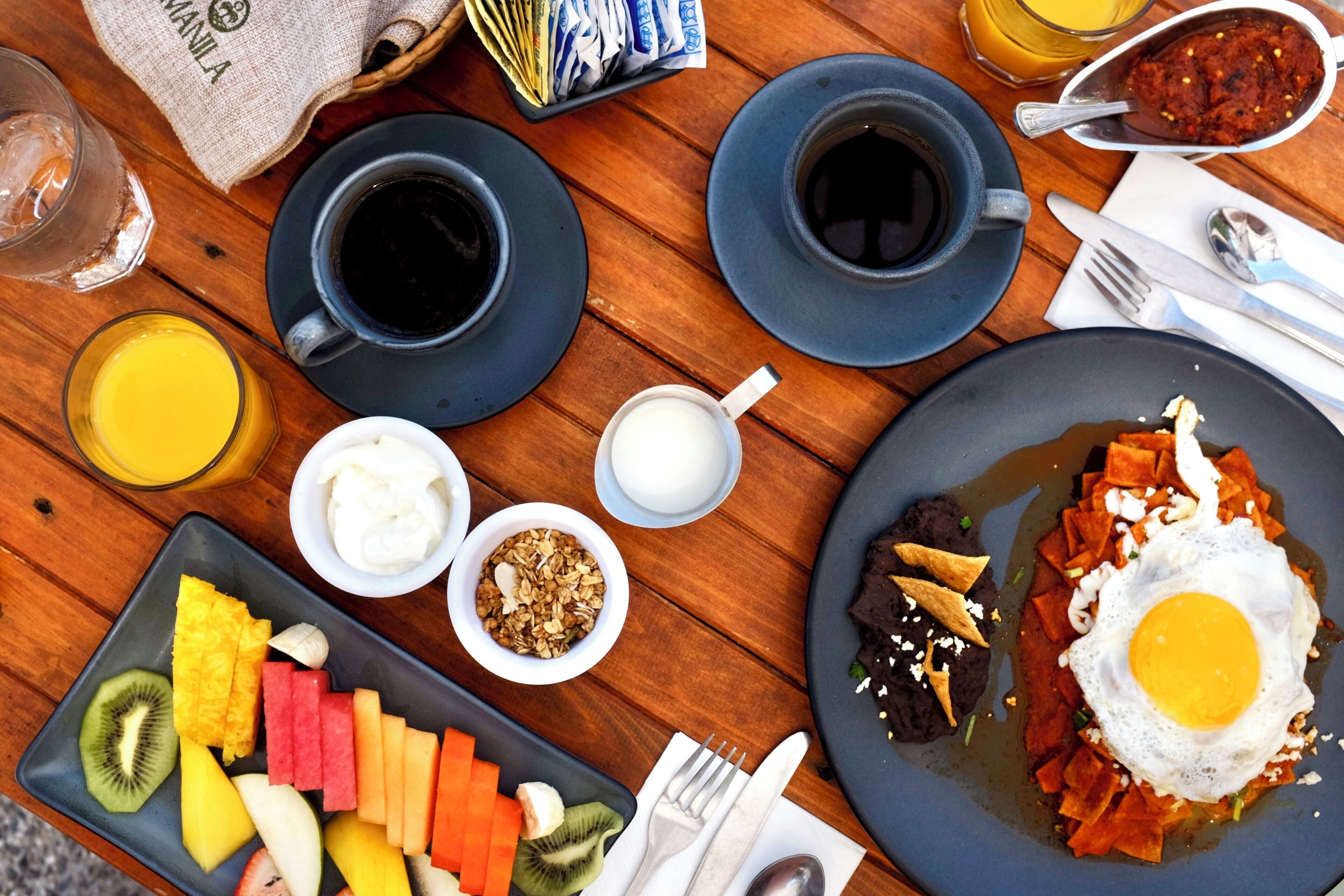 A breakfast table with plates of food, cups of coffee, and a variety of fruits.