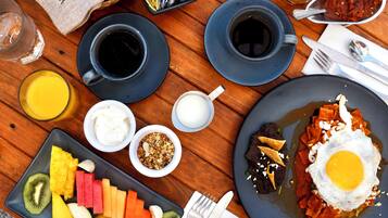 A breakfast table with plates of food, cups of coffee, and a variety of fruits.