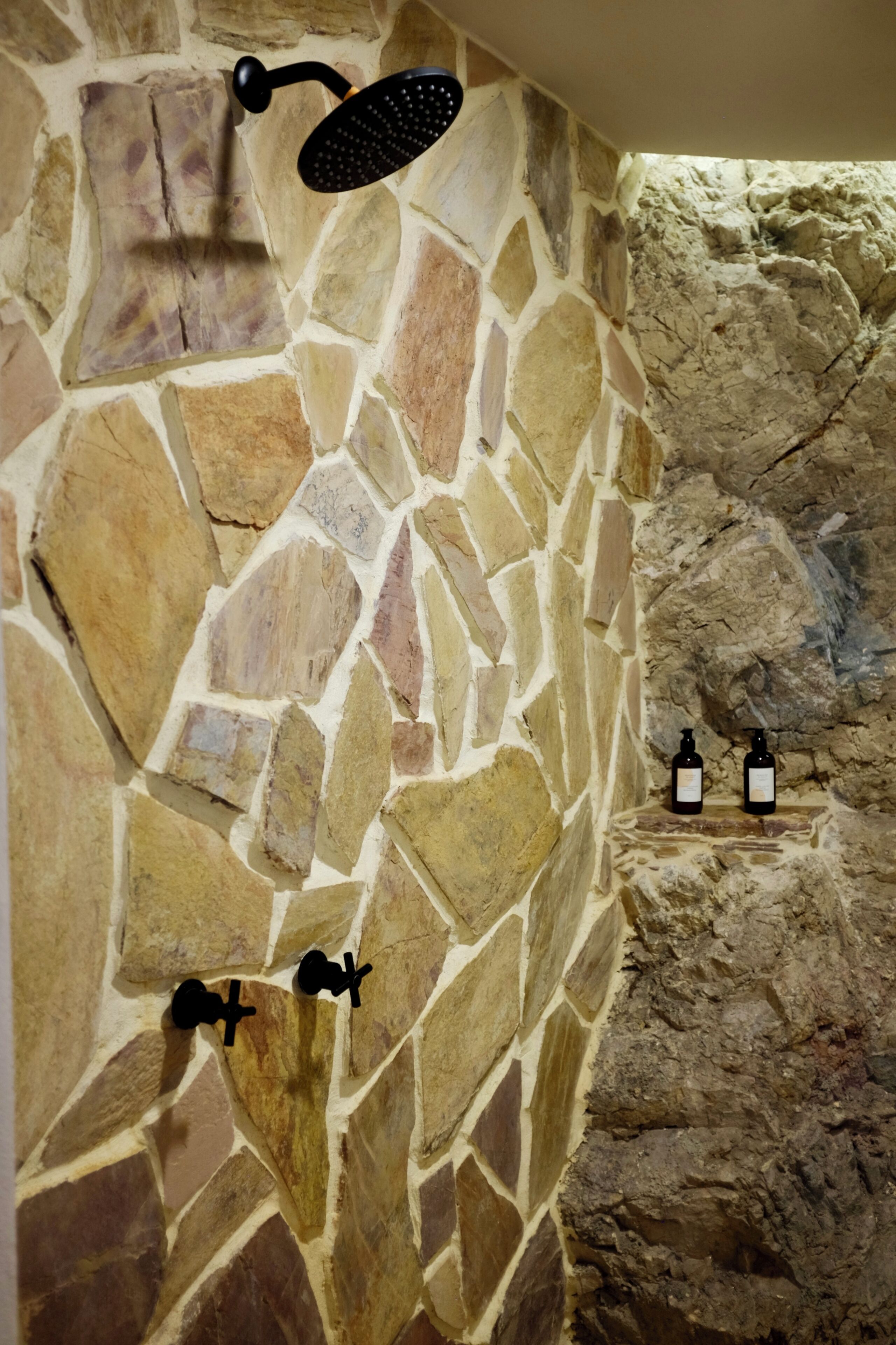 A stone wall with a showerhead and two black fixtures.
