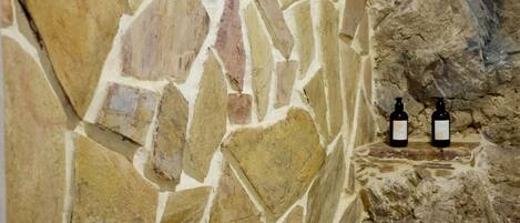 Pared de piedra con cabezal de ducha y dos accesorios negros.