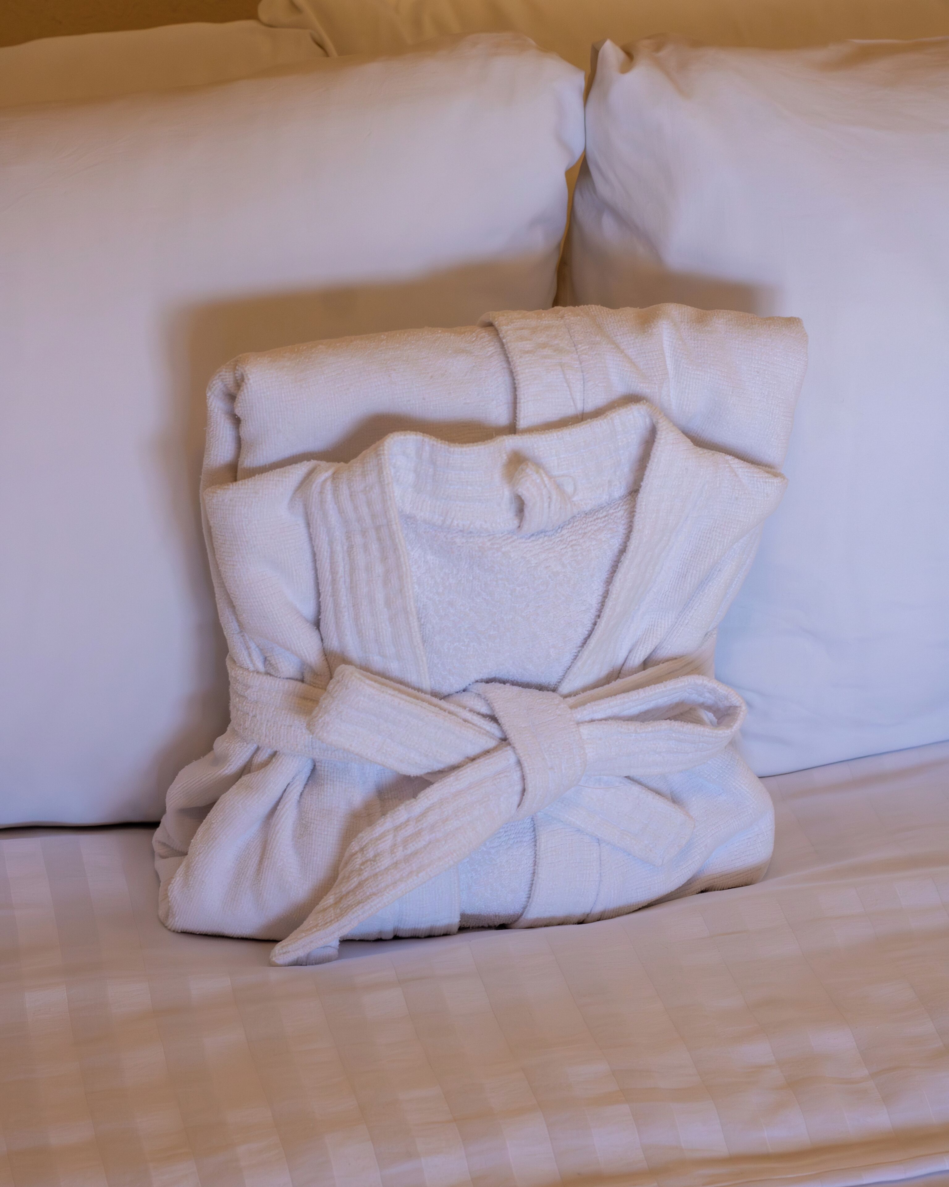 Un peignoir soigneusement plié, maintenu par un ruban, est posé sur un lit recouvert d’une couverture à carreaux.