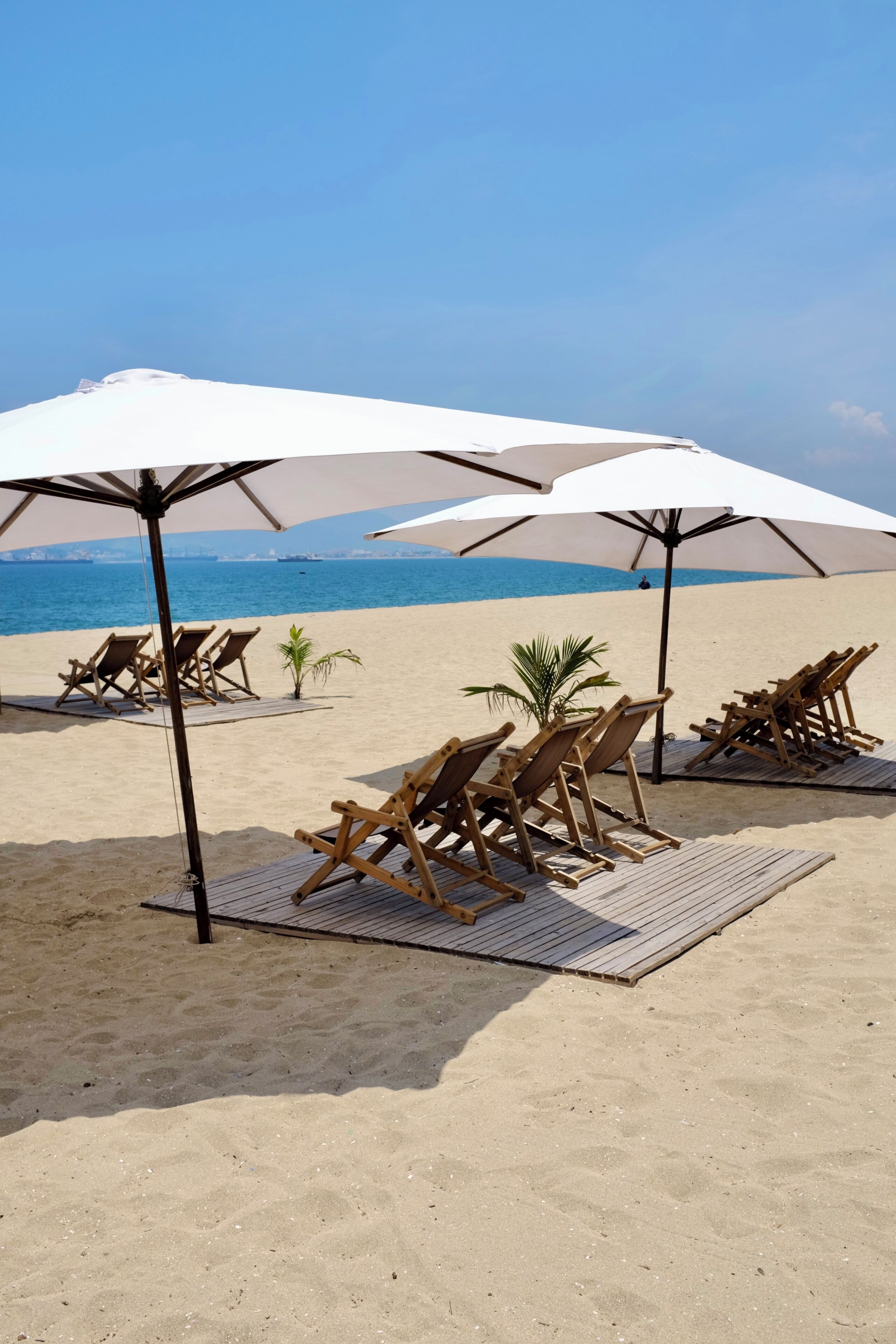Une plage avec des chaises longues en bois et des parasols, un ciel dégagé et une mer calme.