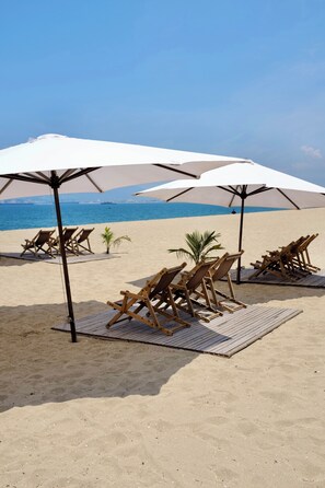 Una playa con sillones de madera y sombrillas, cielo despejado y mar tranquilo.