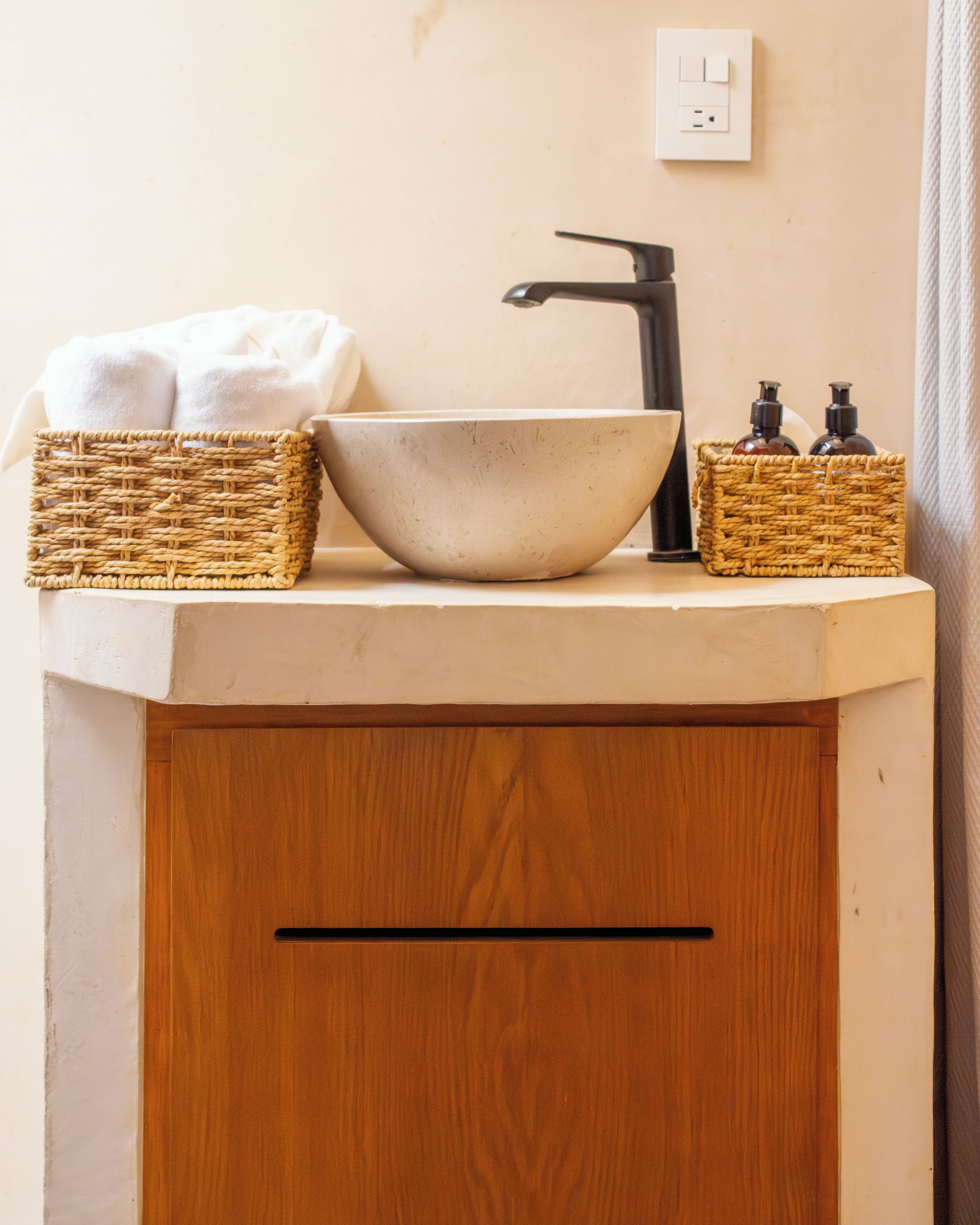 A bathroom with a white sink, a black faucet, and two wicker baskets on the countertop.