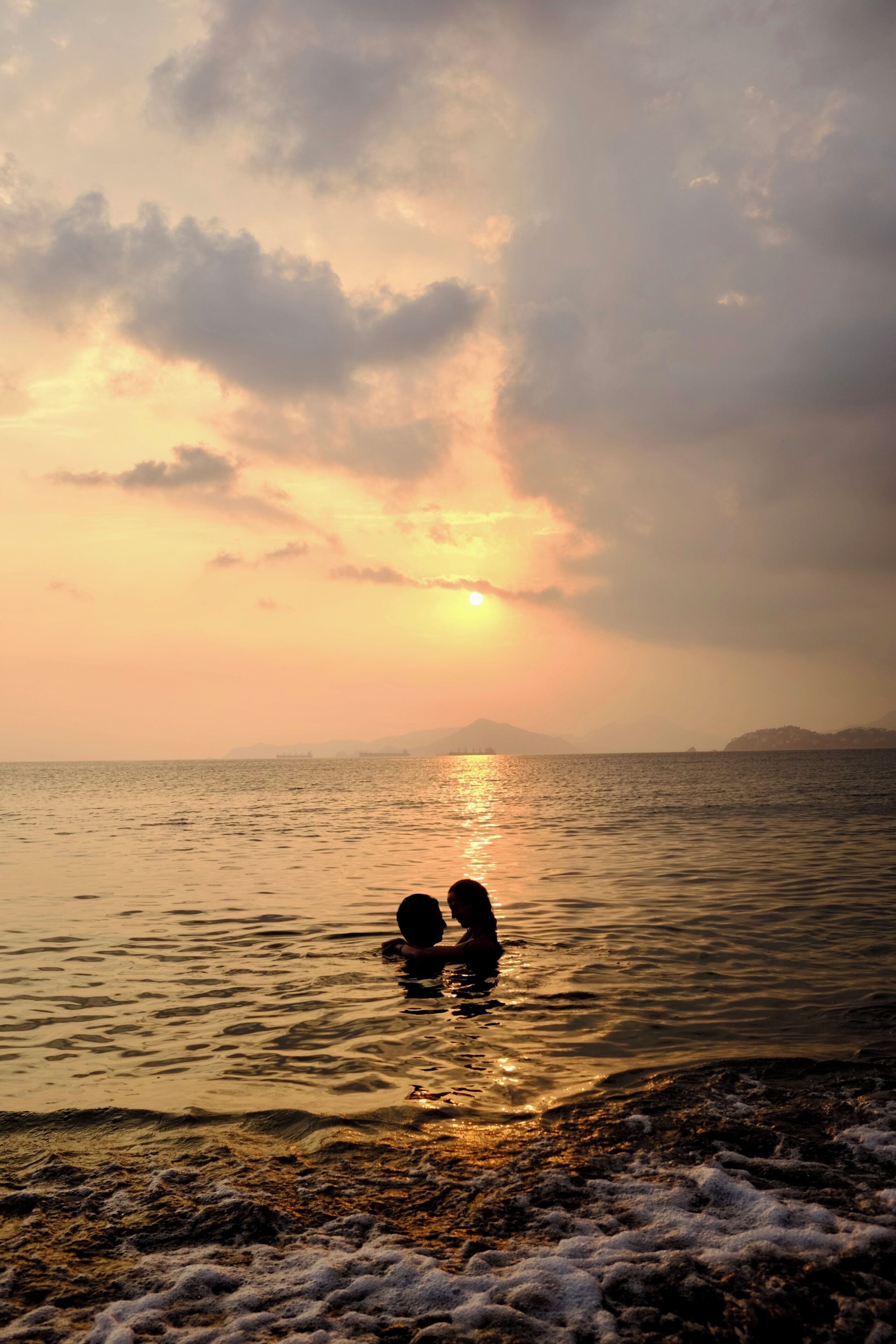 A beach scene with two figures in the water, a sunset, and distant landforms.