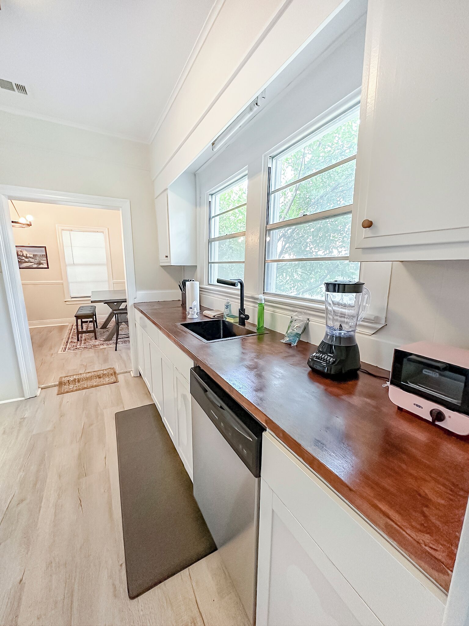 A modern kitchen with white cabinets, a wooden countertop, a built-in dishwasher, a blender, and a toaster.