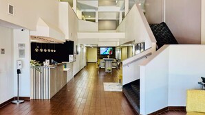 A spacious lobby with a wooden floor, a reception desk, a staircase, and a dining area with a TV screen. - Clarion Pointe (Albemarle)