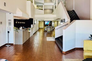 Un vestíbulo espacioso con piso de madera, una mesa de recepción, una escalera y un comedor con una pantalla de televisión.