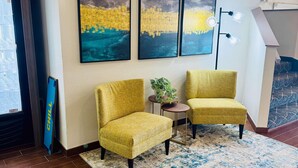A room with two yellow armchairs, a small table with a plant, and three framed artworks on the wall. - Clarion Pointe (Albemarle)