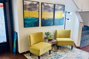 Una habitación con dos sillones amarillos, una mesita con una planta y tres obras de arte enmarcadas en la pared.