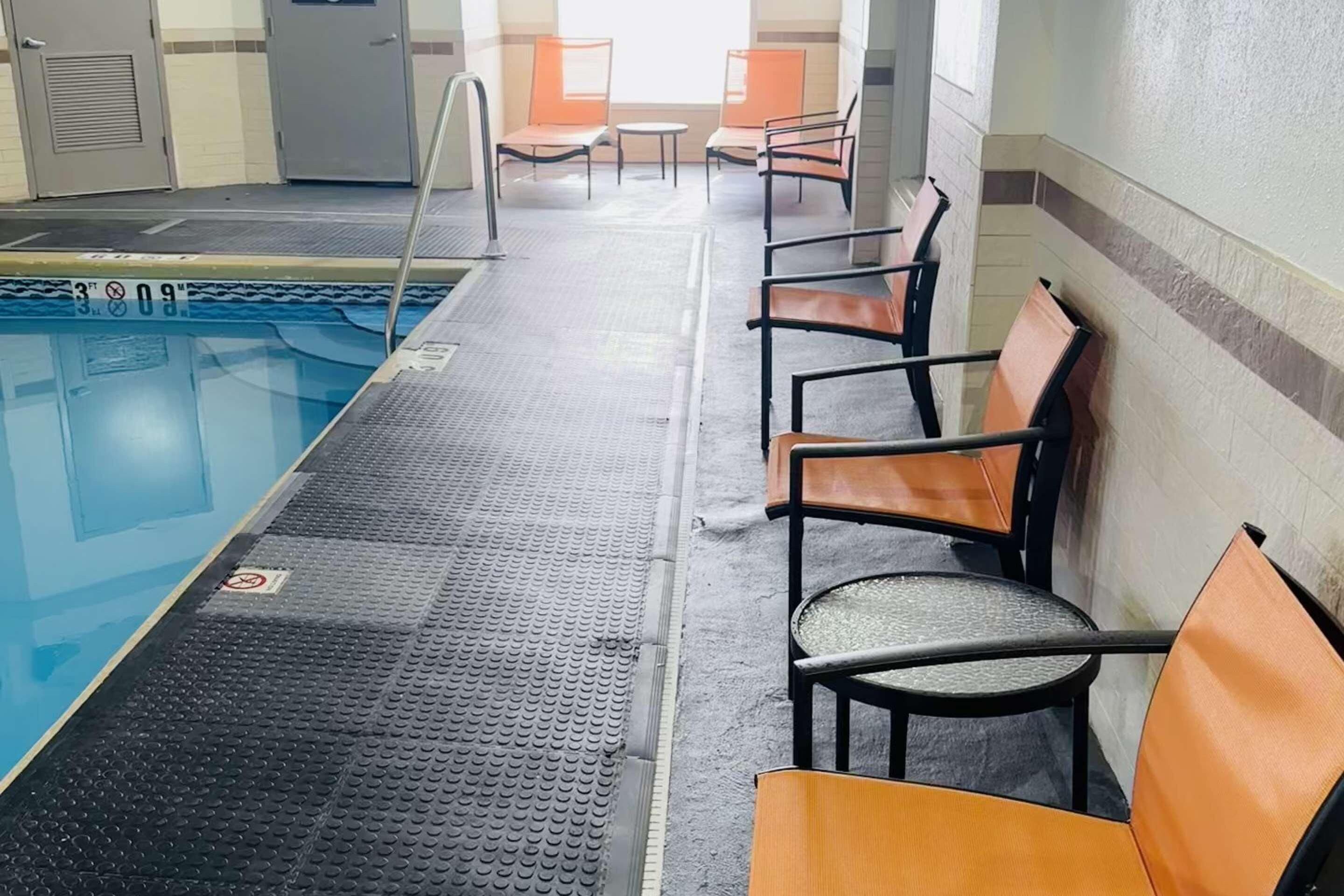 A pool area with a diving board, chairs, and a tiled floor.