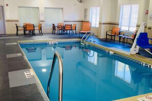 Una piscina con agua cristalina azul, una escalera de piscina y una zona de estar con sillas.