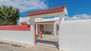 A white building with a red-tiled roof and a red wall. There is a door leading to an outdoor area with a table and chairs.