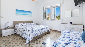 Ein Schlafzimmer mit Bett, Nachttisch, Lampe und einem Gemälde mit Strandmotiv.