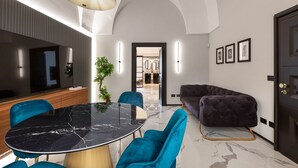 A modern dining area with a marble table, teal chairs, and a dark sofa.