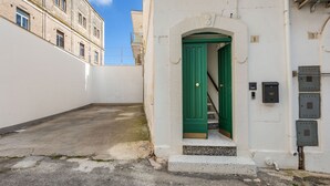 A narrow alleyway with a white building featuring a green door and a small staircase leading to an entrance.
