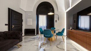 A modern living room with a dark sofa, a round coffee table, teal chairs, and a wooden cabinet with a TV.
