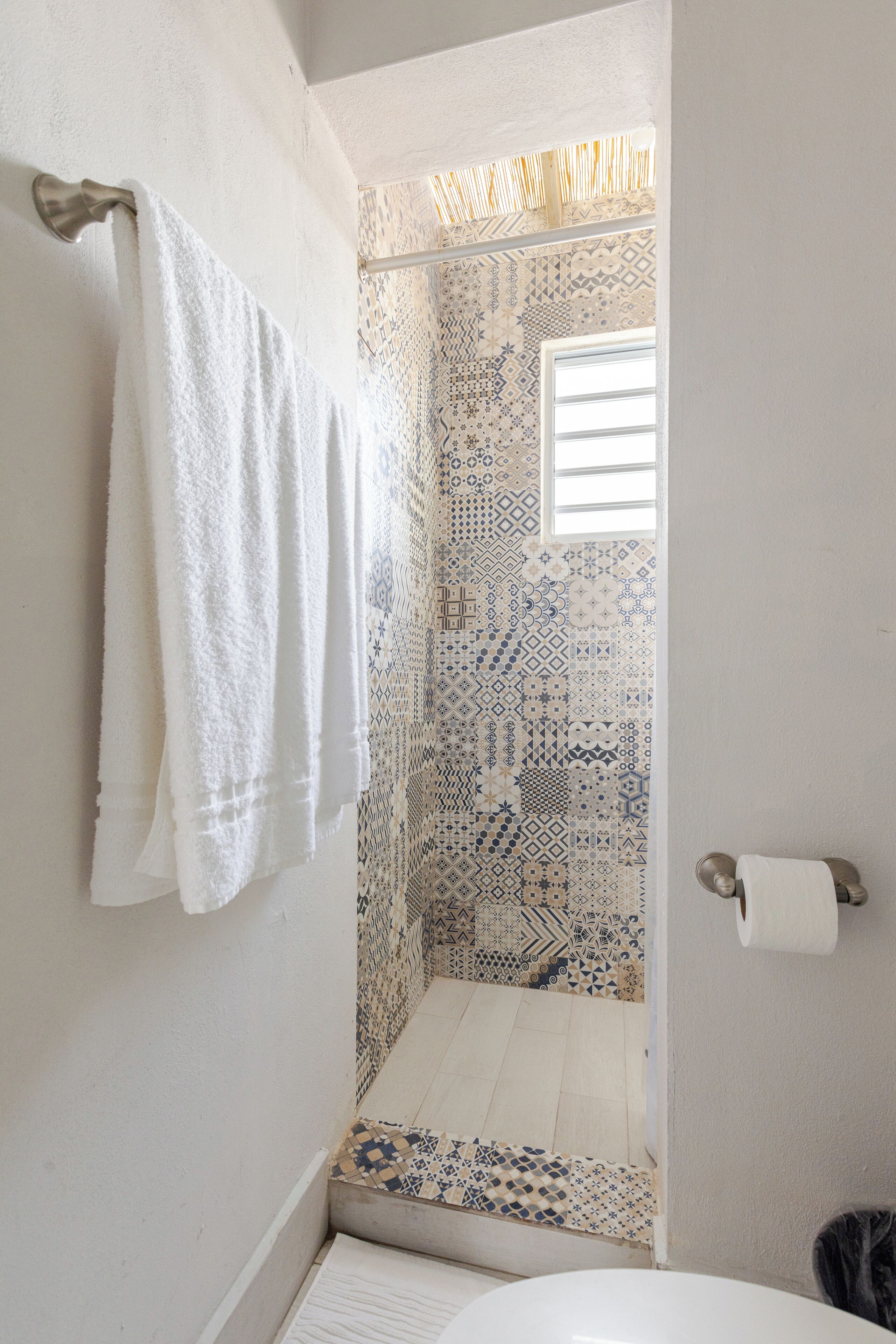 A bathroom with patterned tiles, a white towel hanging on the wall, and a toilet paper holder.