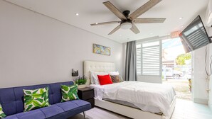 A bedroom with a bed, a sofa, a ceiling fan, and a window with curtains. - City Beach Apartments (San Juan)