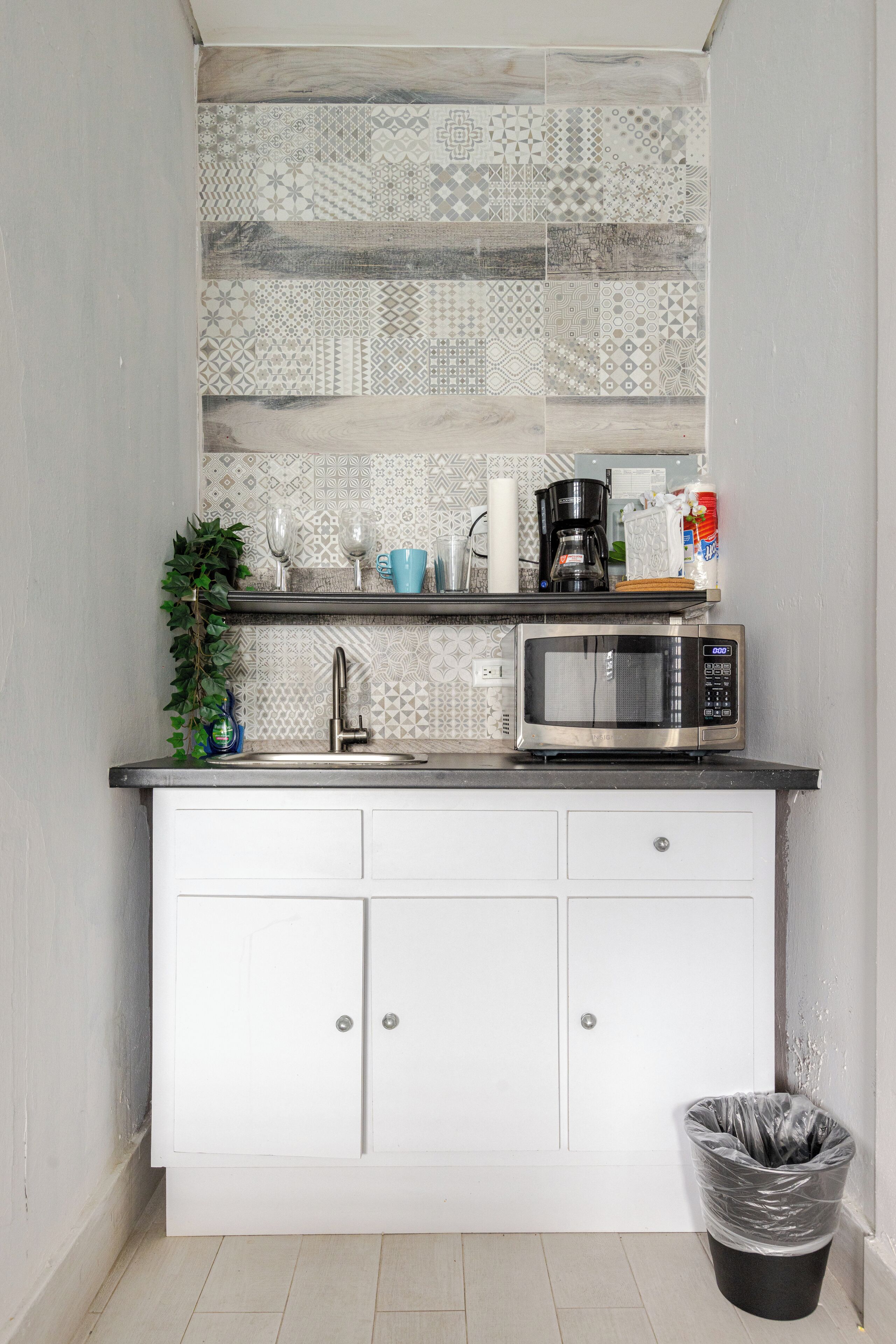 A compact kitchen with a microwave, sink, and white cabinets.