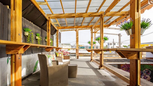A covered outdoor seating area with wicker furniture and potted plants. - City Beach Apartments (San Juan)