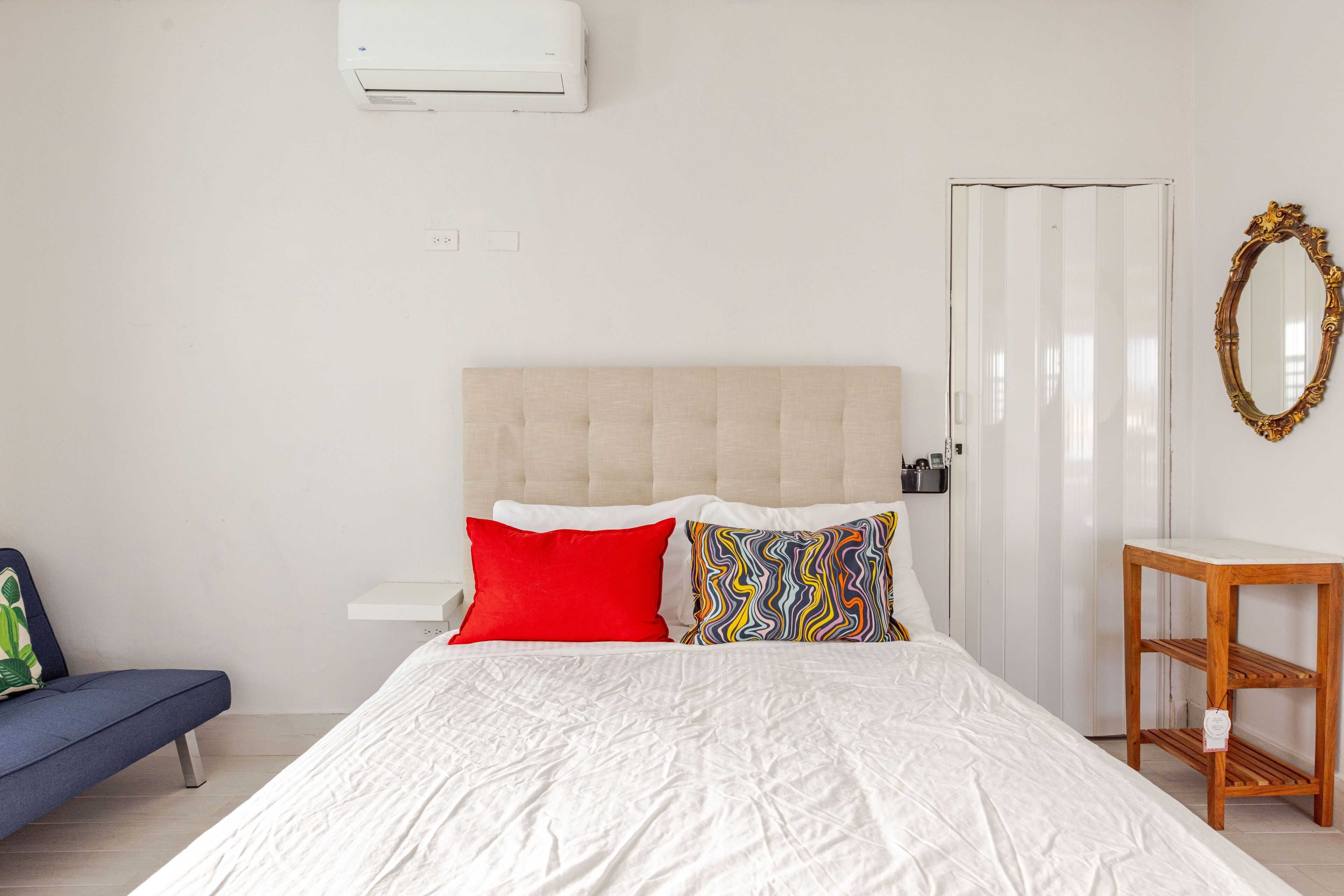 A bedroom with a bed, a bedside table, a mirror, and a blue chair.