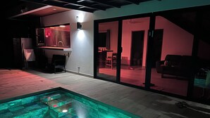 A modern indoor pool with a geometric design, a dining area with a red-lit ambiance, and a visible staircase leading to another level.