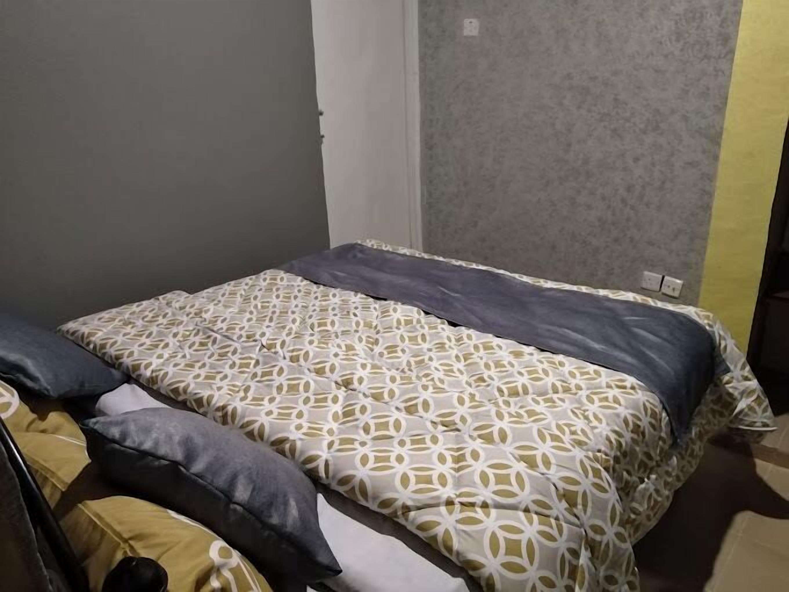 A bedroom with a bed, pillows, and a grey patterned wall.