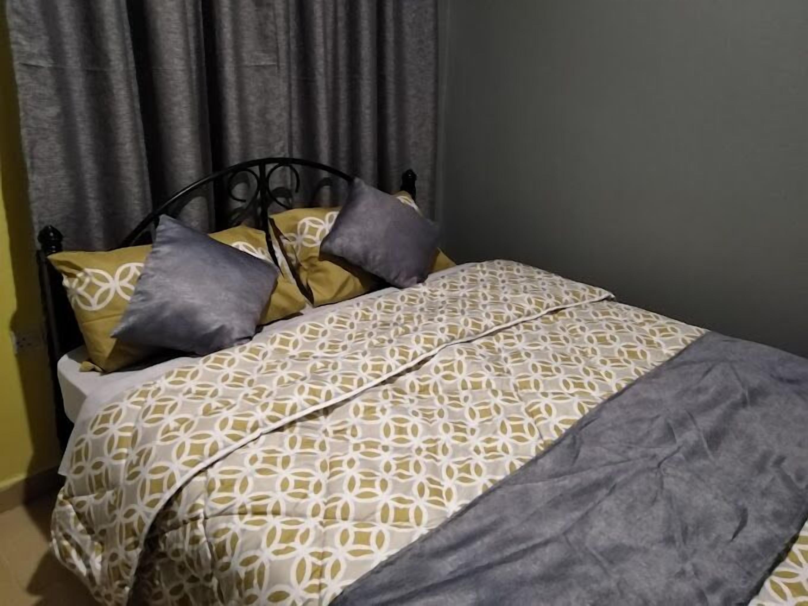 Una cama con una colcha estampada, almohadas y una manta gris.