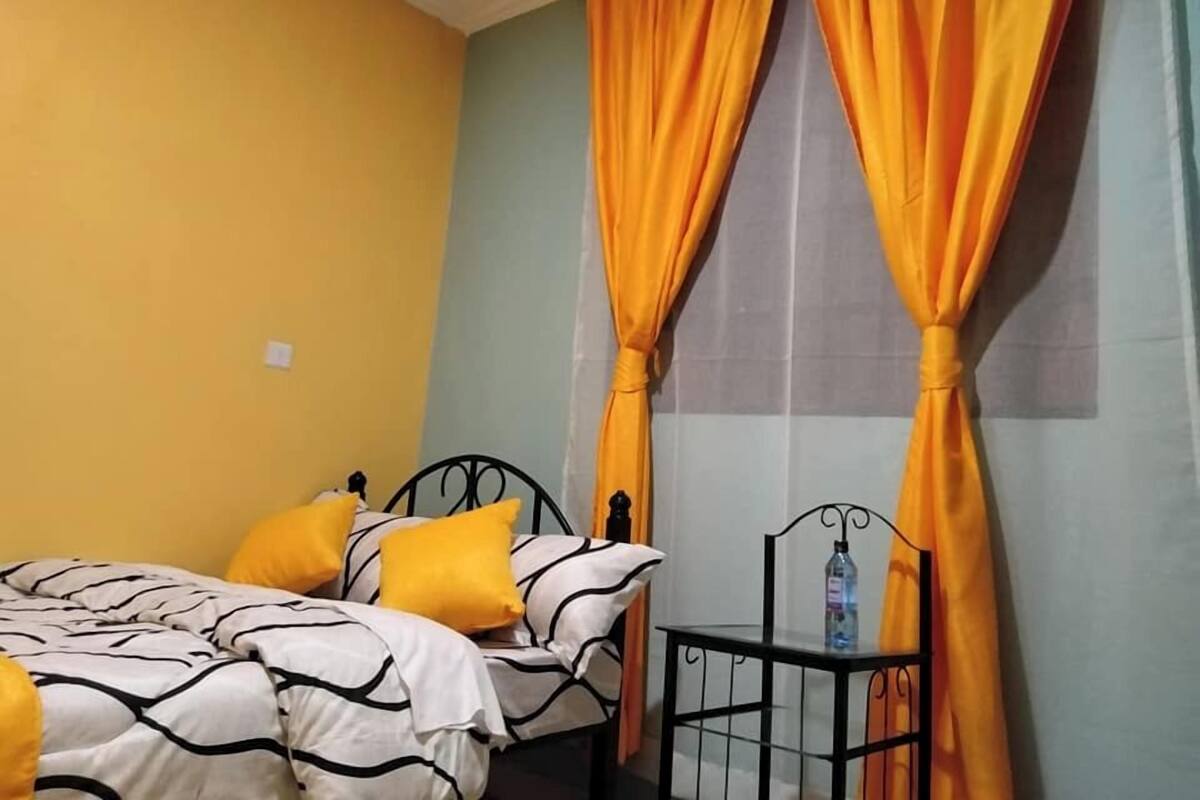 A room with a bed, yellow pillows, and orange curtains.