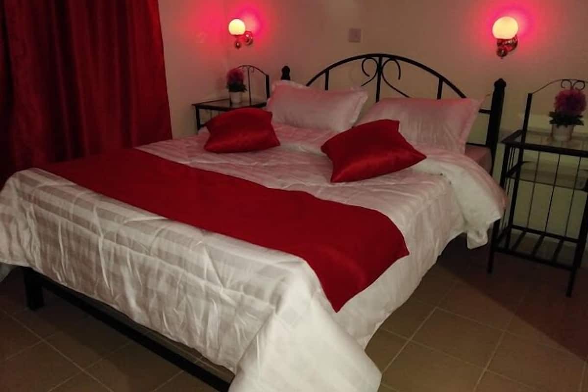 A bed with white and red bedding, two red pillows, and two wall-mounted lamps.