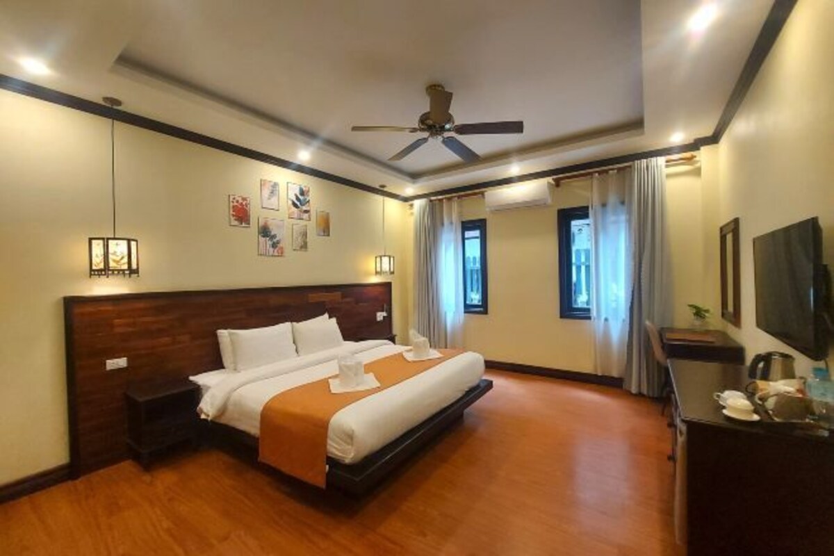 A hotel room with a large bed, a ceiling fan, a desk with a chair, and a television.