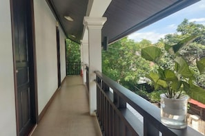 Un balcon abrité, agrémenté d’un pot de fleurs, d’une balustrade et offrant une vue sur la verdure.