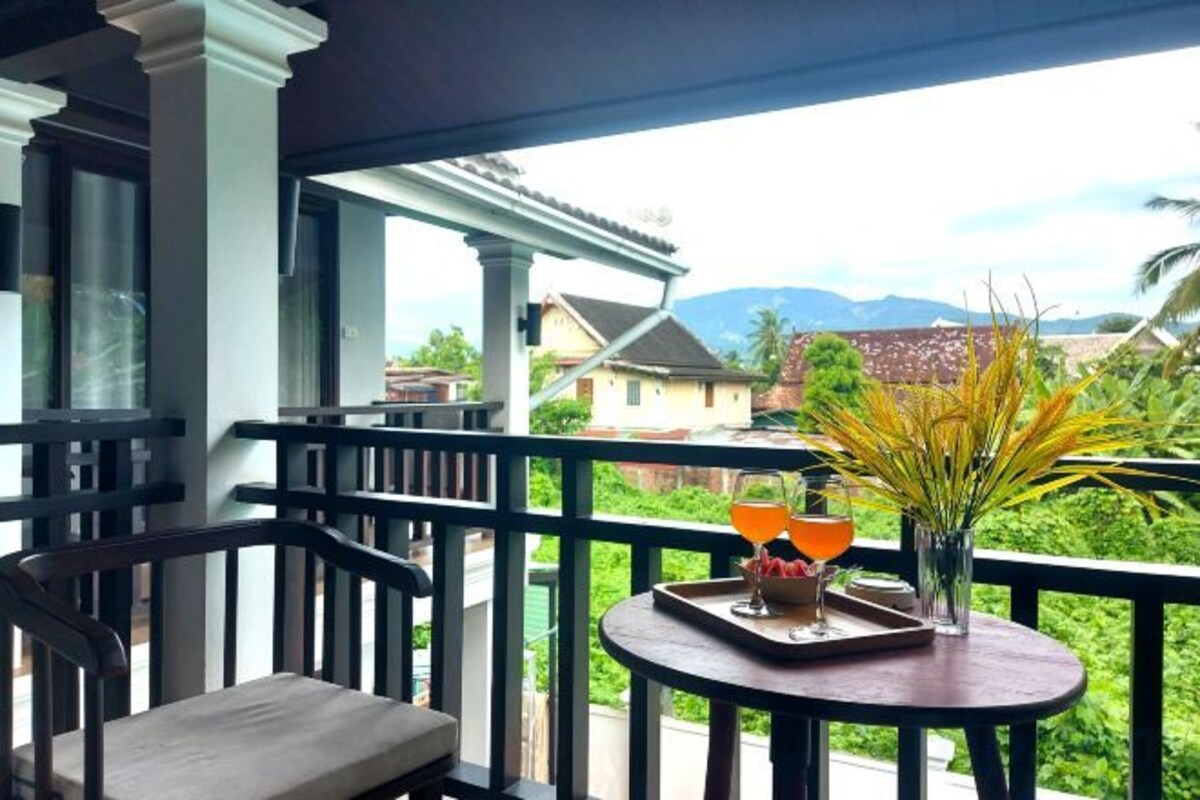 Un balcon avec une table, une chaise et une vue sur une maison et des montagnes.
