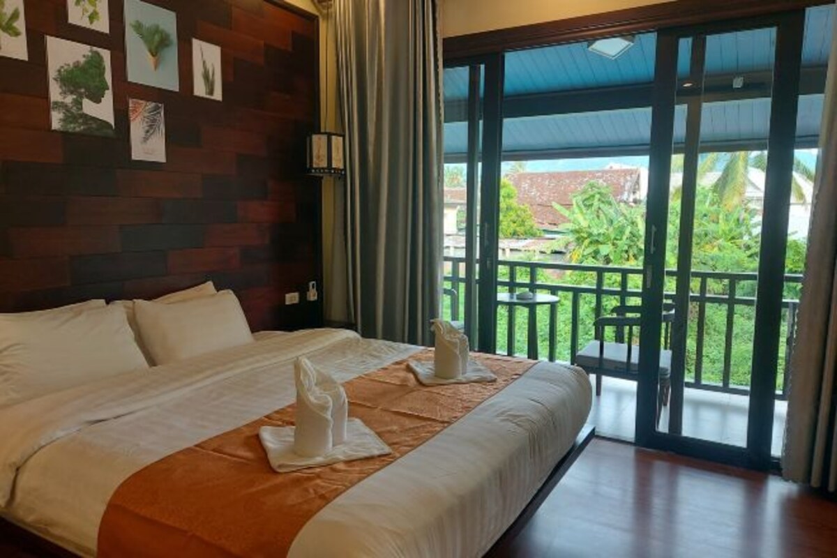 A hotel room with a large bed, a balcony with a view of greenery, and wall art.