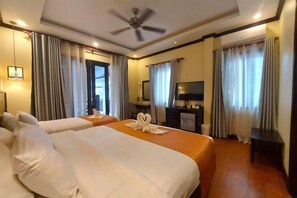 Une chambre d’hôtel avec deux lits, un ventilateur de plafond, un bureau avec une chaise, une télévision et des rideaux.