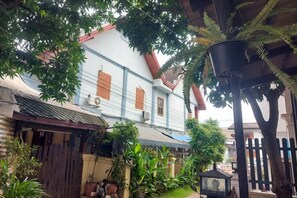 Un bâtiment traditionnel avec un toit en tuiles, une clôture en bois et une variété de plantes en pot.