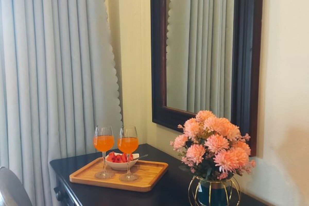 A table with two glasses of orange beverage, a bowl of fruit, and a vase of flowers.